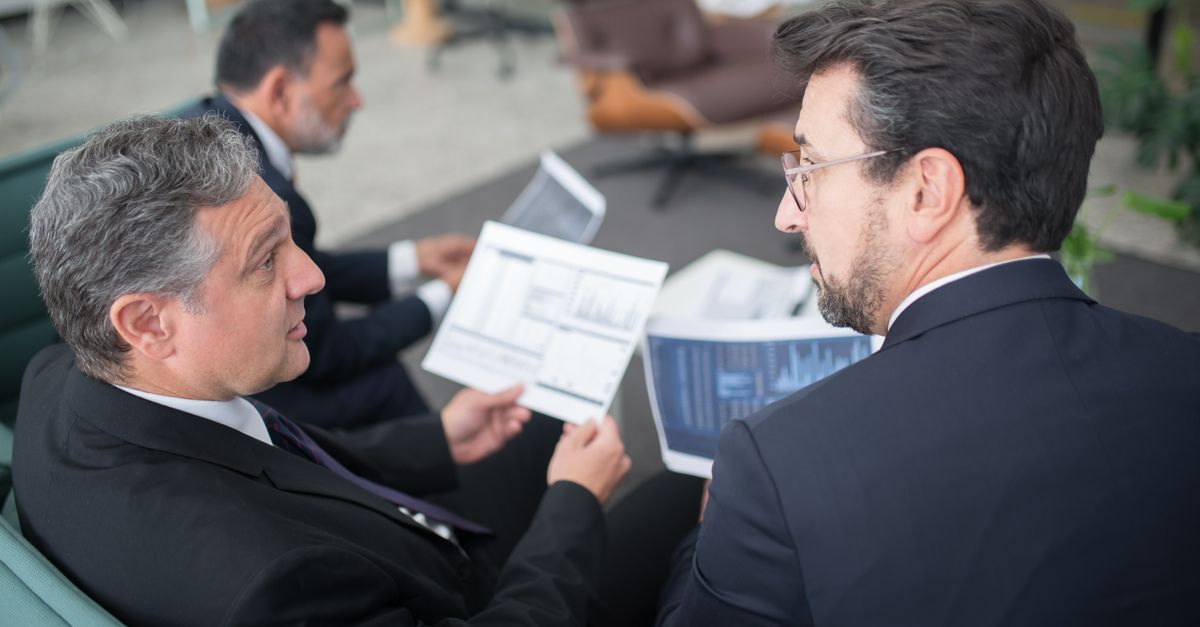Three businessmen discussing financial documents in a modern office setting.