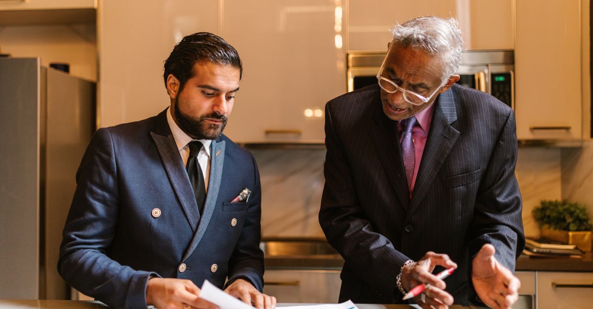 Two business professionals in suits reviewing printed documents together.