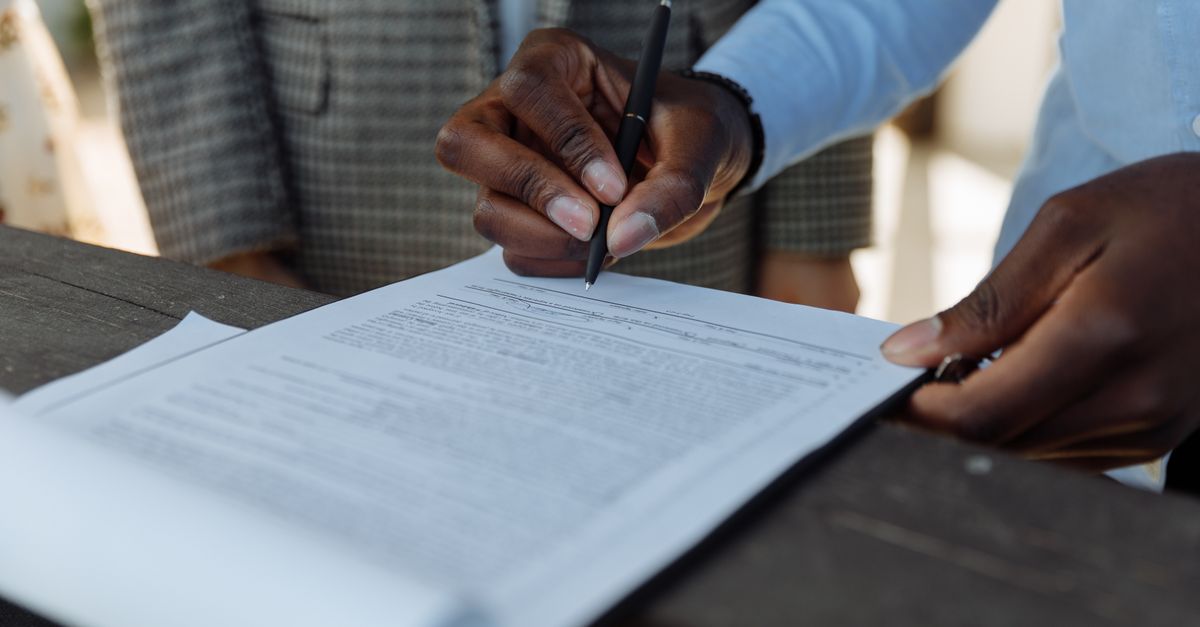 Close-up of business professionals signing a document with a pen indoors.
