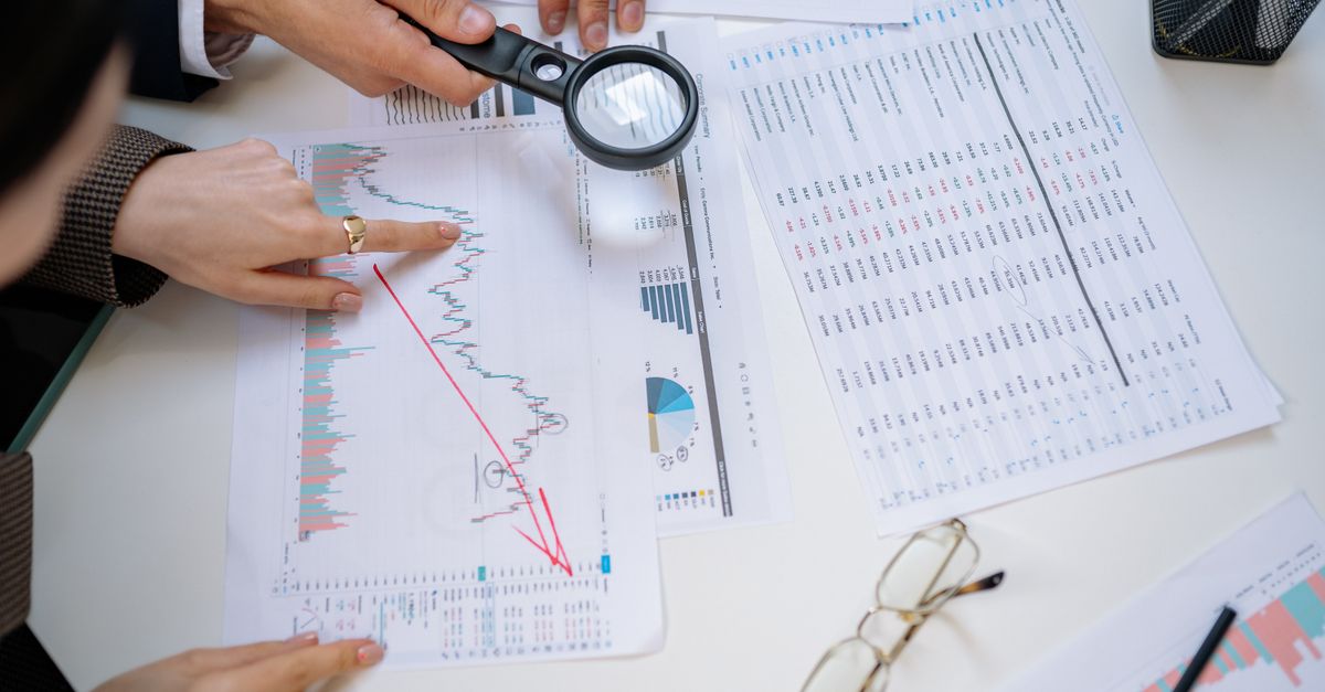 Business professionals examining financial documents with magnifying glass for detailed analysis.