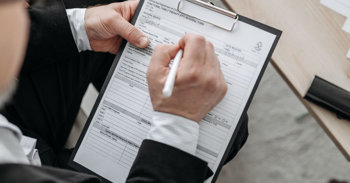 Close-up of a businessman signing a formal document on a clipboard.