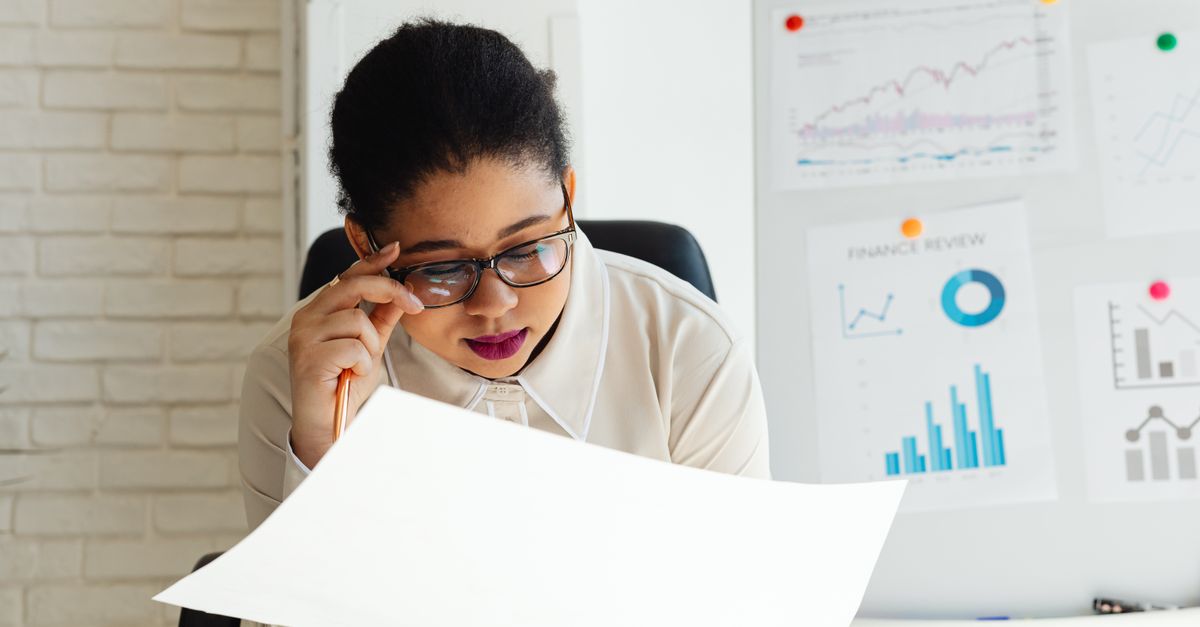 Focused businesswoman examining financial reports with graphs and charts on a whiteboard.
